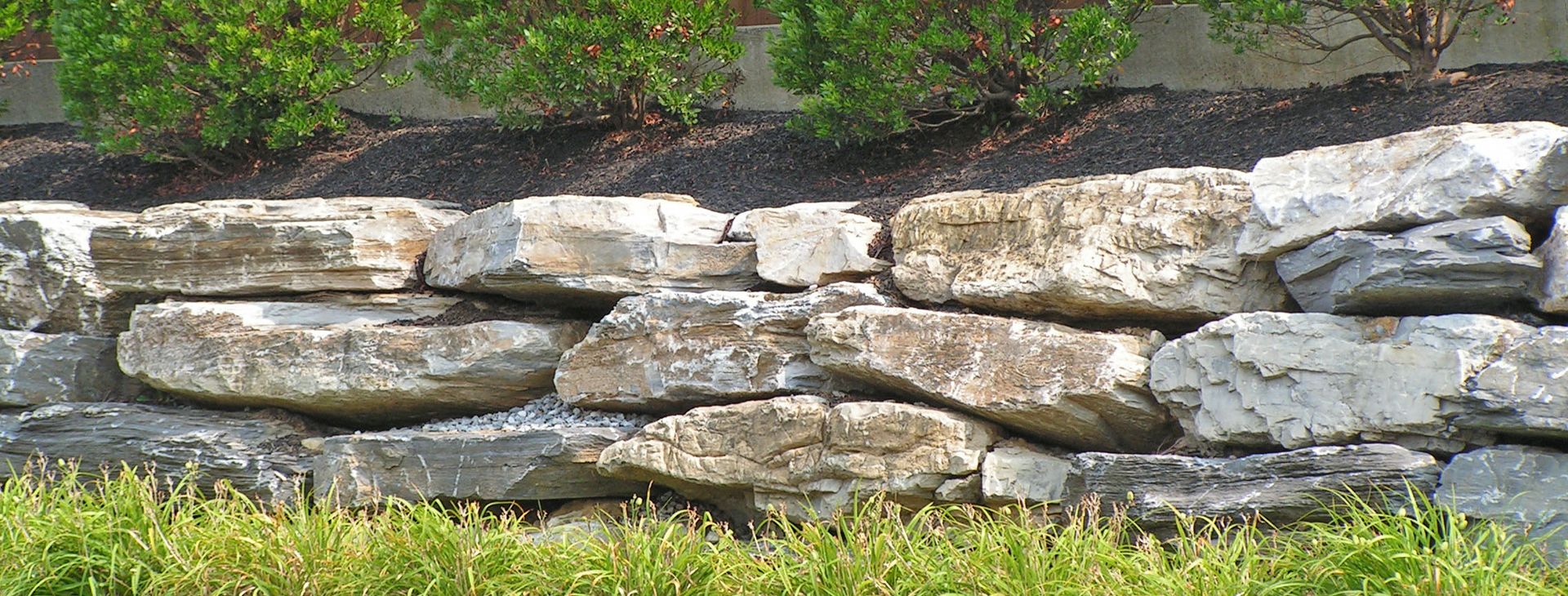 Natural boulder retaining wall with a garden bed above and lawn below
