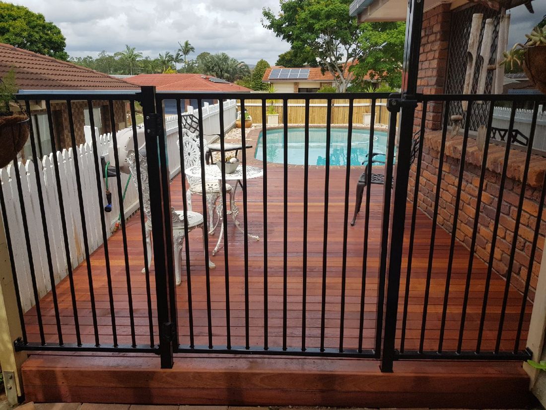 Hardwood deck beside a pool behind black pool fencing