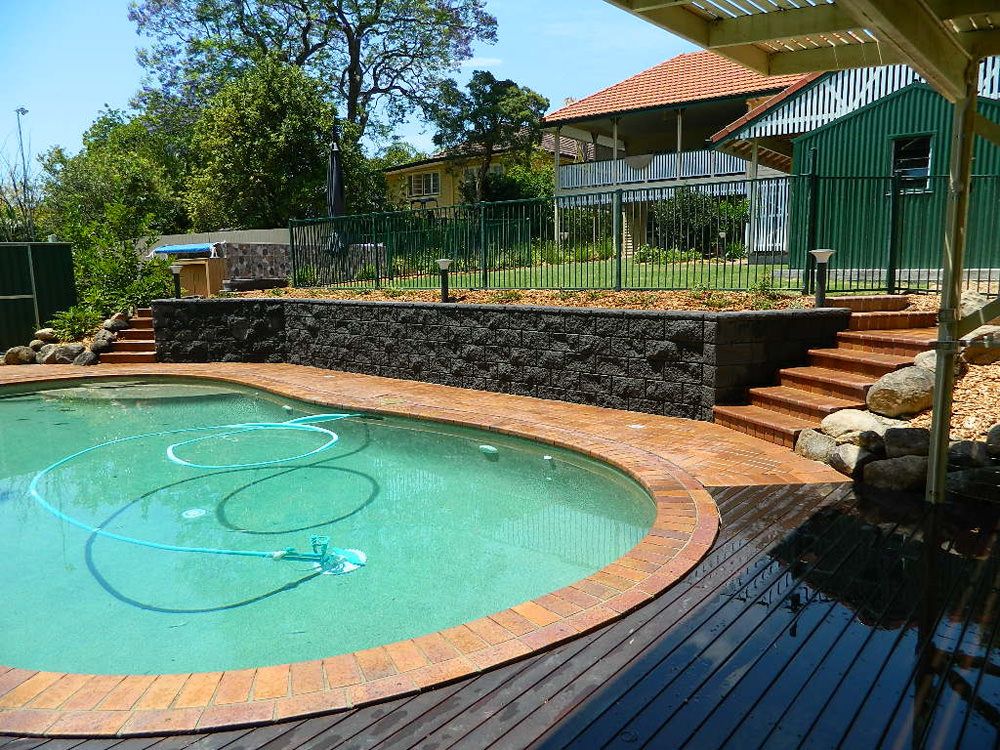 Pool with timber deck and steps up to a stone wall