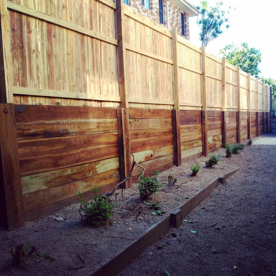 Timber sleeper boundary retaining wall below a fence