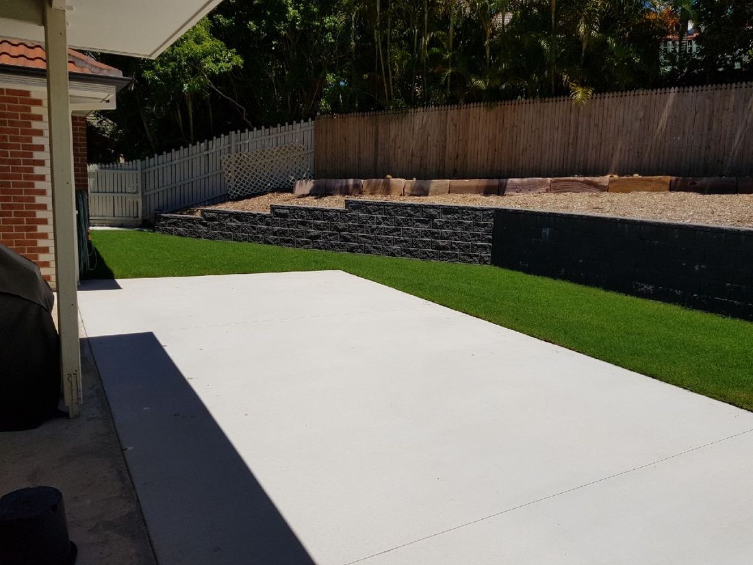 New block retaining wall with lawn above and a fresh concrete slab below